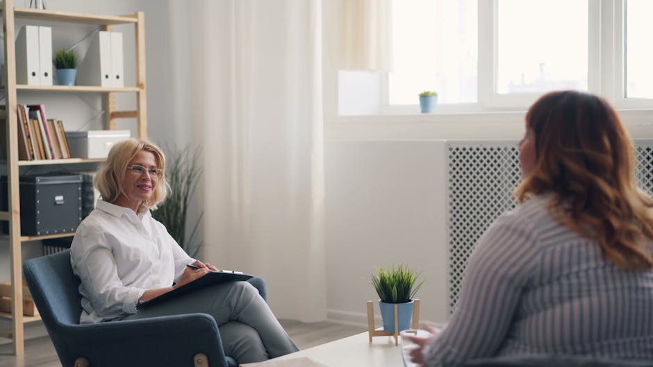Two women in conversation during a therapy-style consultation in a bright room.